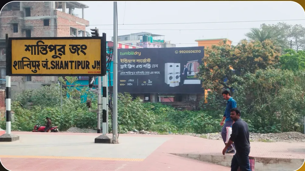 Tumbledry hoarding in Bengali beside the Shantipur Junction station sign